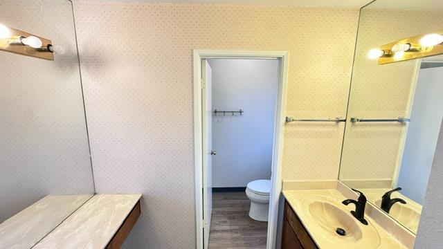 5455 N Marty Ave Unit 111, Fresno, CA 93711 - bathroom with vanity, toilet, wood finished floors, and wallpapered walls