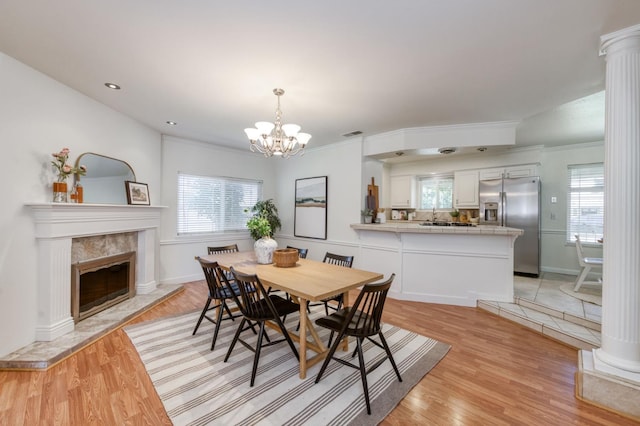 5753 N 7th St, Fresno, CA 93710 - dining space featuring light wood-style flooring, a chandelier, a high end fireplace, decorative columns, and crown molding