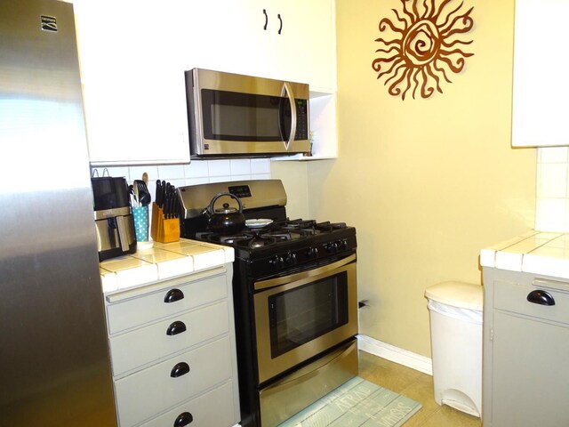 4457 E Brown Ave, Fresno, CA 93703 - kitchen with appliances with stainless steel finishes, tile counters, tasteful backsplash, and light tile patterned flooring