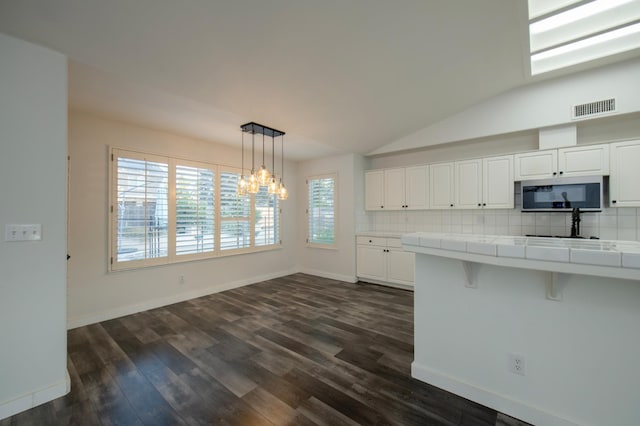 10485 N Sinclair Cir, Fresno, CA 93730 - kitchen with tile counters, stainless steel microwave, white cabinetry, a chandelier, and vaulted ceiling