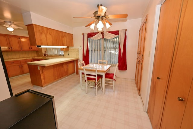 1911 W Simpson Ave, Fresno, CA 93705 - kitchen featuring a ceiling fan, a peninsula, brown cabinets, decorative backsplash, and light countertops