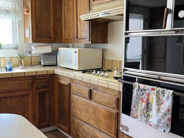 1173 Menlo Ave, Clovis, CA 93612 - kitchen with under cabinet range hood, white microwave, tile countertops, and brown cabinetry