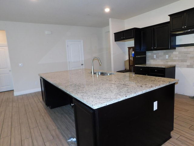 5875 E Pitt Ave, Fresno, CA 93727 - kitchen with a sink, dark cabinets, light stone countertops, light wood finished floors, and tasteful backsplash