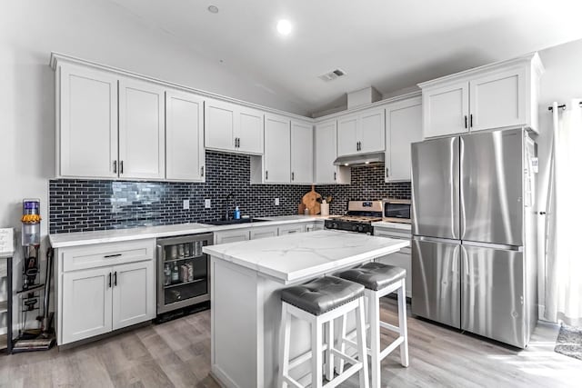 22375 Fairmead Cir, Chowchilla, CA 93610 - kitchen featuring stainless steel appliances, wine cooler, under cabinet range hood, light wood-type flooring, and backsplash