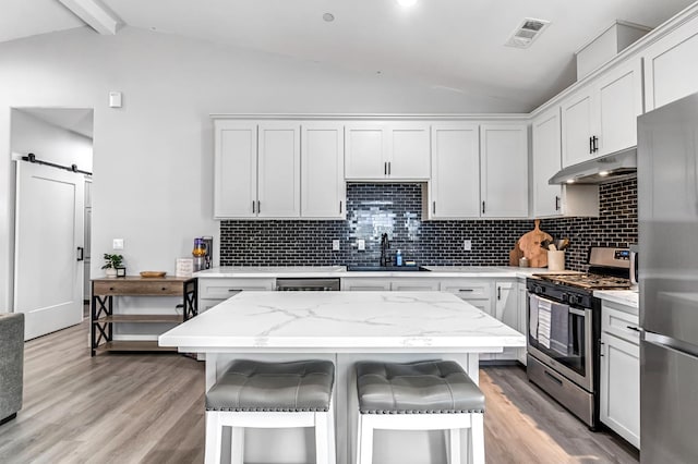 22375 Fairmead Cir, Chowchilla, CA 93610 - kitchen with stainless steel appliances, under cabinet range hood, a kitchen breakfast bar, light wood-type flooring, and decorative backsplash