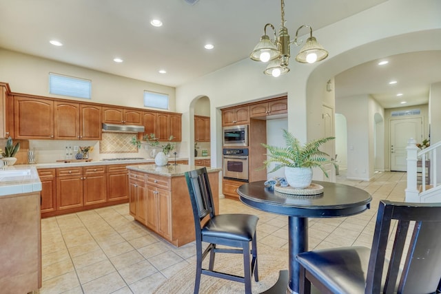 3202 Everglade Ave, Clovis, CA 93619 - kitchen with arched walkways, appliances with stainless steel finishes, under cabinet range hood, light tile patterned flooring, and tasteful backsplash