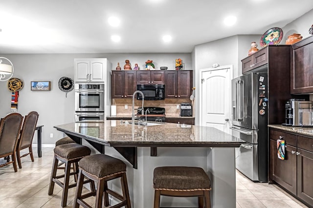 976 Daisy Ct, Dinuba, CA 93618 - kitchen featuring stainless steel appliances, a breakfast bar, light tile patterned floors, dark stone countertops, and decorative backsplash