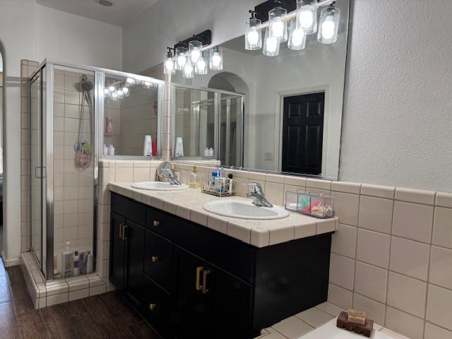 2400 Garda Corte, Chowchilla, CA 93610 - bathroom featuring double vanity, a shower stall, tile walls, wood finished floors, and a textured wall