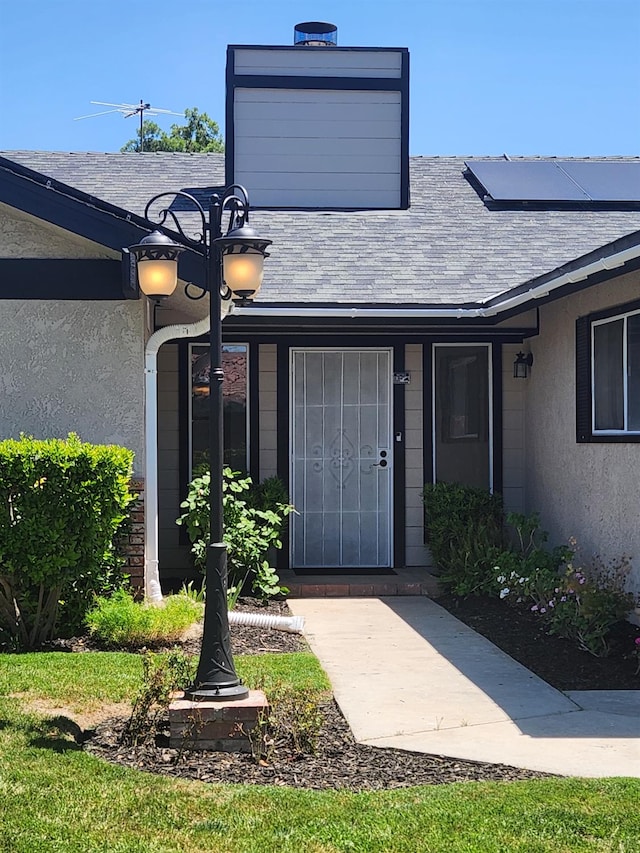 6536 N Tracy Ave, Fresno, CA 93722 - doorway to property with roof mounted solar panels, stucco siding, and a shingled roof