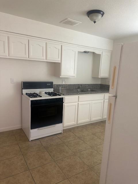 2967 E Iowa Ave, Fresno, CA 93701 - kitchen featuring range with gas stovetop, freestanding refrigerator, white cabinets, and tile patterned flooring