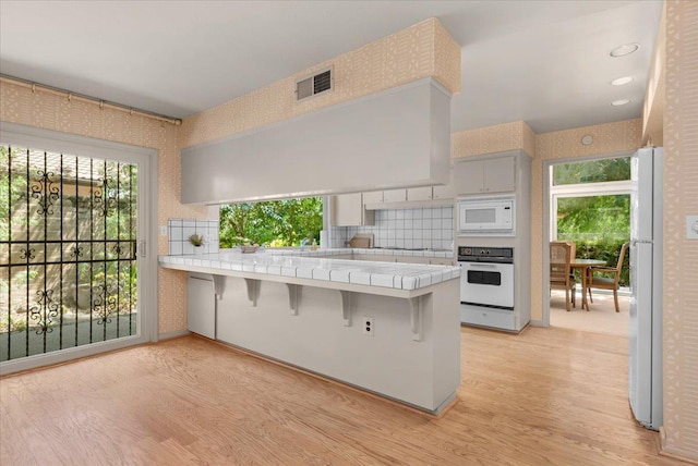 5532 N El Adobe Dr, Fresno, CA 93711 - kitchen featuring white appliances, wallpapered walls, tile countertops, a peninsula, and light wood-type flooring
