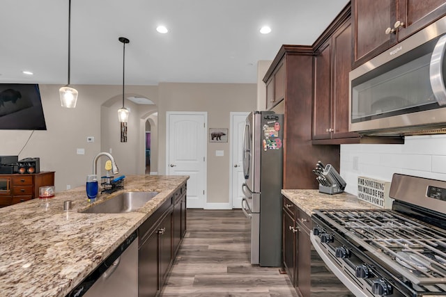 1160 Summit Ct, Madera, CA 93638 - kitchen featuring stainless steel appliances, arched walkways, light stone countertops, dark wood finished floors, and dark brown cabinetry