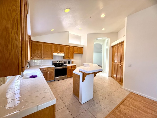 4688 W Weldon Ave, Fresno, CA 93722 - kitchen with stainless steel range with electric cooktop, tile counters, under cabinet range hood, arched walkways, and lofted ceiling