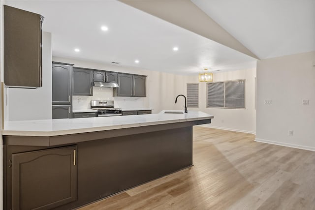 2540 E Seeger Ave, Visalia, CA 93292 - kitchen with stainless steel range with gas cooktop, under cabinet range hood, a peninsula, backsplash, and light wood-type flooring