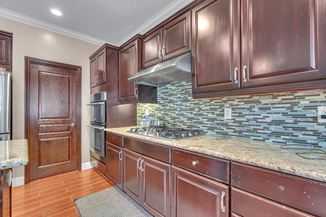 3017 W Oleander Ave, Fresno, CA 93706 - kitchen featuring appliances with stainless steel finishes, under cabinet range hood, ornamental molding, backsplash, and light wood-style flooring