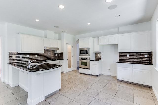 1090 Clara Ave, Fowler, CA 93625 - kitchen featuring appliances with stainless steel finishes, dark countertops, under cabinet range hood, decorative backsplash, and white cabinetry