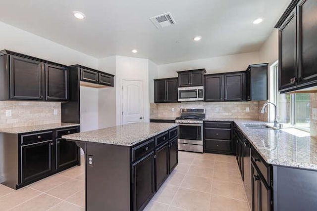 2166 Junipero Ave, Clovis, CA 93619 - kitchen featuring appliances with stainless steel finishes, light stone counters, backsplash, a kitchen island, and light tile patterned floors