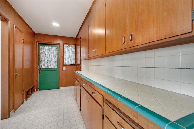 5481 E Geary St, Fresno, CA 93727 - kitchen with tile countertops, brown cabinets, tasteful backsplash, and wood walls