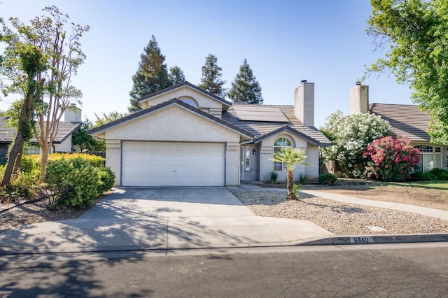 9340 N Jackson Ave, Fresno, CA 93720 - ranch-style house featuring driveway, an attached garage, stucco siding, roof mounted solar panels, and a tiled roof