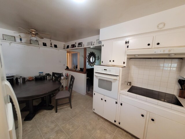 kitchen featuring oven, ceiling fan, tile counters, backsplash, and white cabinets