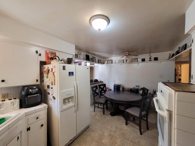 kitchen with white refrigerator with ice dispenser, tile counters, ceiling fan, white cabinets, and stove