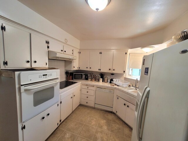 kitchen featuring white appliances, under cabinet range hood, decorative backsplash, and white cabinetry