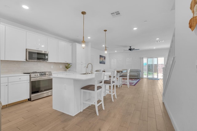 6569 E Lyell Ave, Fresno, CA 93727 - kitchen with stainless steel appliances, open floor plan, tasteful backsplash, light wood-style flooring, and white cabinets