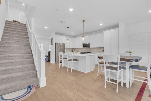 6569 E Lyell Ave, Fresno, CA 93727 - kitchen featuring appliances with stainless steel finishes, white cabinetry, light countertops, a kitchen breakfast bar, and light wood-type flooring