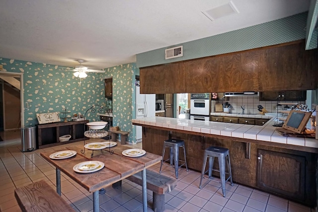 5513 N El Adobe Dr, Fresno, CA 93711 - kitchen with tile counters, wallpapered walls, white appliances, light tile patterned floors, and ceiling fan