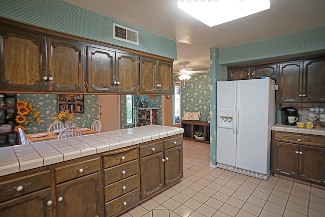 5513 N El Adobe Dr, Fresno, CA 93711 - kitchen featuring white fridge with ice dispenser, wallpapered walls, light tile patterned floors, tile countertops, and a ceiling fan