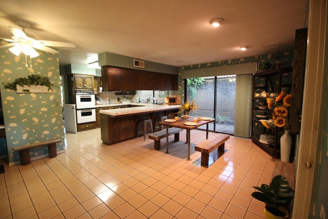 5513 N El Adobe Dr, Fresno, CA 93711 - kitchen with a peninsula, light tile patterned floors, white double oven, light countertops, and ceiling fan