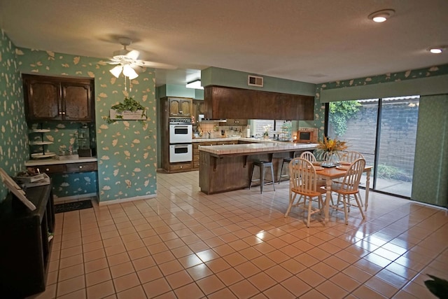 5513 N El Adobe Dr, Fresno, CA 93711 - kitchen featuring white double oven, wallpapered walls, a peninsula, light countertops, and ceiling fan