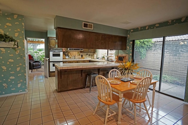 5513 N El Adobe Dr, Fresno, CA 93711 - kitchen with tile counters, wallpapered walls, double oven, a peninsula, and light tile patterned floors