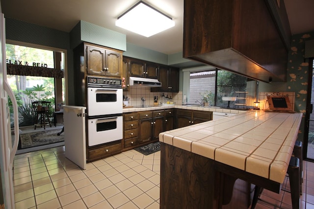 5513 N El Adobe Dr, Fresno, CA 93711 - kitchen featuring white appliances, under cabinet range hood, dark brown cabinetry, light tile patterned flooring, and backsplash