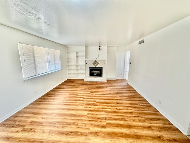535 W Peralta Way, Fresno, CA 93705 - unfurnished living room featuring light wood-style flooring, a tiled fireplace, and built in shelves
