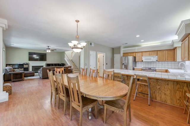 7718 N Constance Ave, Fresno, CA 93722 - dining room with ceiling fan, light wood-style flooring, a fireplace, and stairs