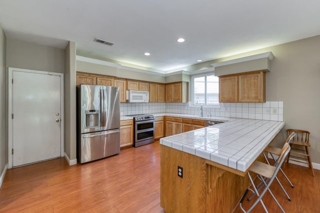 7718 N Constance Ave, Fresno, CA 93722 - kitchen featuring appliances with stainless steel finishes, a peninsula, a breakfast bar, light wood-type flooring, and tasteful backsplash