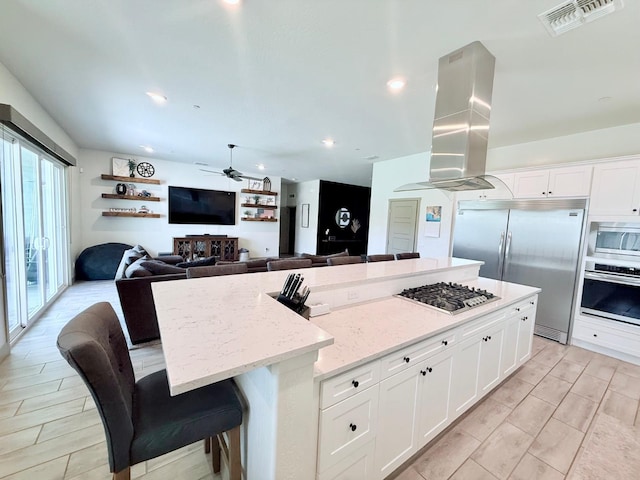 825 Spring St W, Madera, CA 93636 - kitchen with built in appliances, island exhaust hood, a center island, a ceiling fan, and white cabinetry
