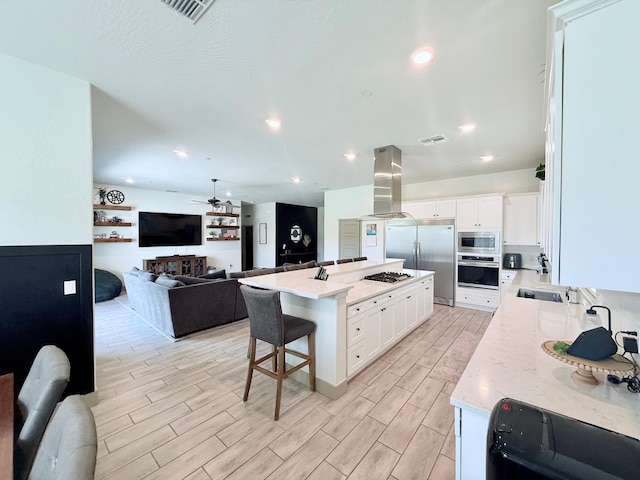 825 Spring St W, Madera, CA 93636 - kitchen featuring built in appliances, island range hood, a ceiling fan, a breakfast bar area, and white cabinets