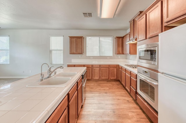 5516 N Sebastian Ln, Fresno, CA 93722 - kitchen with stainless steel appliances, tile counters, light wood-type flooring, under cabinet range hood, and brown cabinets