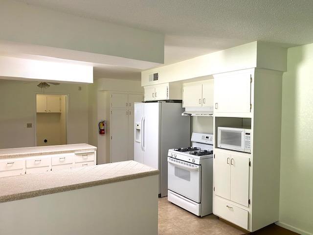 4902 E Townsend Ave, Fresno, CA 93727 - kitchen with white appliances, white cabinets, light countertops, and under cabinet range hood