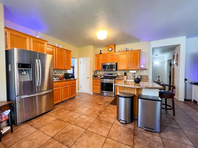 2518 Keats Ave, Fresno, CA 93611 - kitchen featuring appliances with stainless steel finishes, a peninsula, a breakfast bar, light tile patterned flooring, and brown cabinets