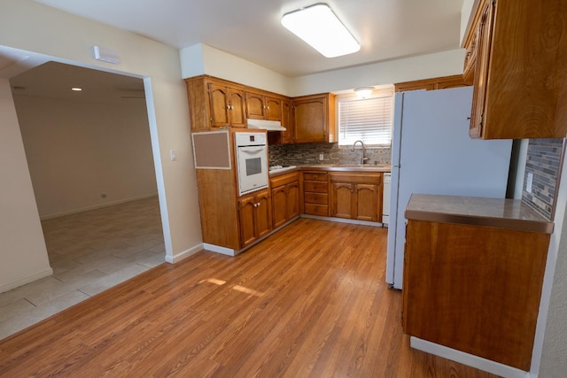 2739 Fine Ave, Clovis, CA 93612 - kitchen featuring white appliances, brown cabinets, under cabinet range hood, backsplash, and light wood-type flooring