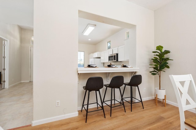 9416 N Jade Ave, Fresno, CA 93720 - kitchen featuring stainless steel microwave, freestanding refrigerator, a kitchen breakfast bar, white cabinetry, and light countertops