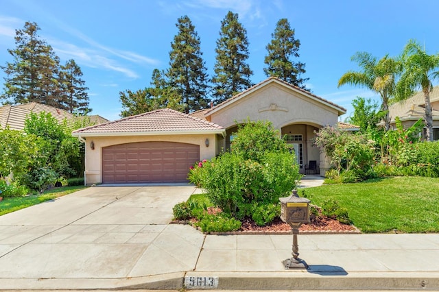 5613 W Bluff Ave, Fresno, CA 93722 - mediterranean / spanish home featuring stucco siding, a garage, a tile roof, concrete driveway, and a front lawn