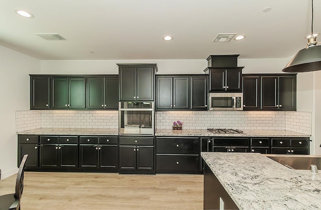 117 Emperor Way, Dinuba, CA 93618 - kitchen featuring appliances with stainless steel finishes, dark cabinetry, light wood-style floors, light stone counters, and recessed lighting