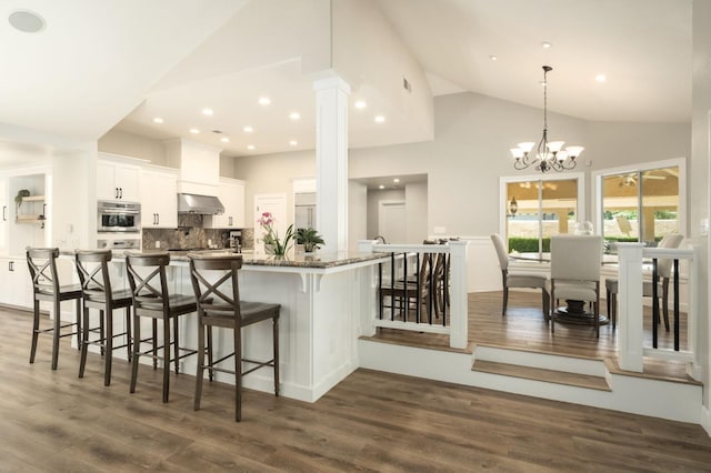 7671 N Ricewood Ave, Fresno, CA 93711 - kitchen featuring extractor fan, high vaulted ceiling, a breakfast bar area, white cabinetry, and decorative backsplash