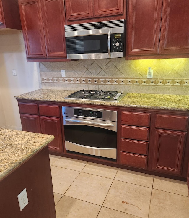 3310 N Jason Ave, Fresno, CA 93737 - kitchen with appliances with stainless steel finishes, reddish brown cabinets, decorative backsplash, light stone countertops, and light tile patterned flooring