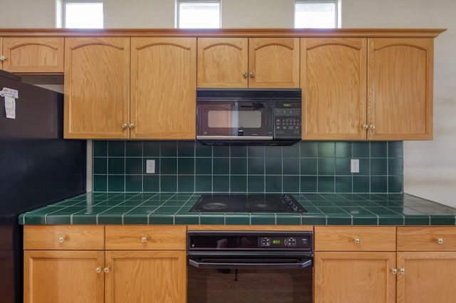 7515 N Wheeler Ave, Fresno, CA 93722 - kitchen with black appliances, tile countertops, backsplash, and light brown cabinetry