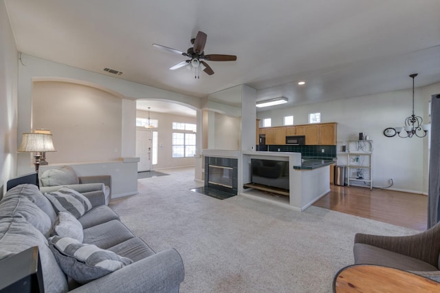 7515 N Wheeler Ave, Fresno, CA 93722 - living room with arched walkways, a chandelier, a ceiling fan, carpet flooring, and a tiled fireplace